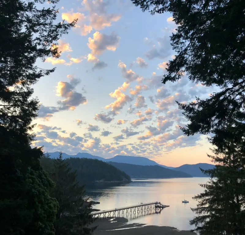 A dock reaching into Howe Sound at sunset, seen through Gambier Island forest