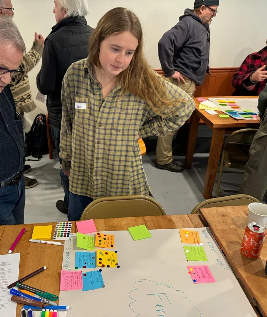 Sam Wing at a community workshop, looking over a board of sticky-note ideas on a table with residents around her